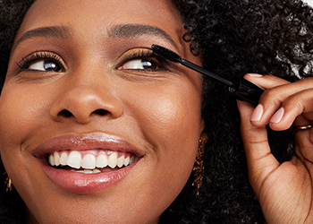 A woman applies ultimate mascara to her lashes while smiling.